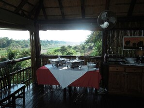 A dining area with a table set for service, a fan, and a view of a lush landscape.
