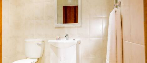 Un baño con inodoro, lavamanos y una toalla colgada en un perchero.