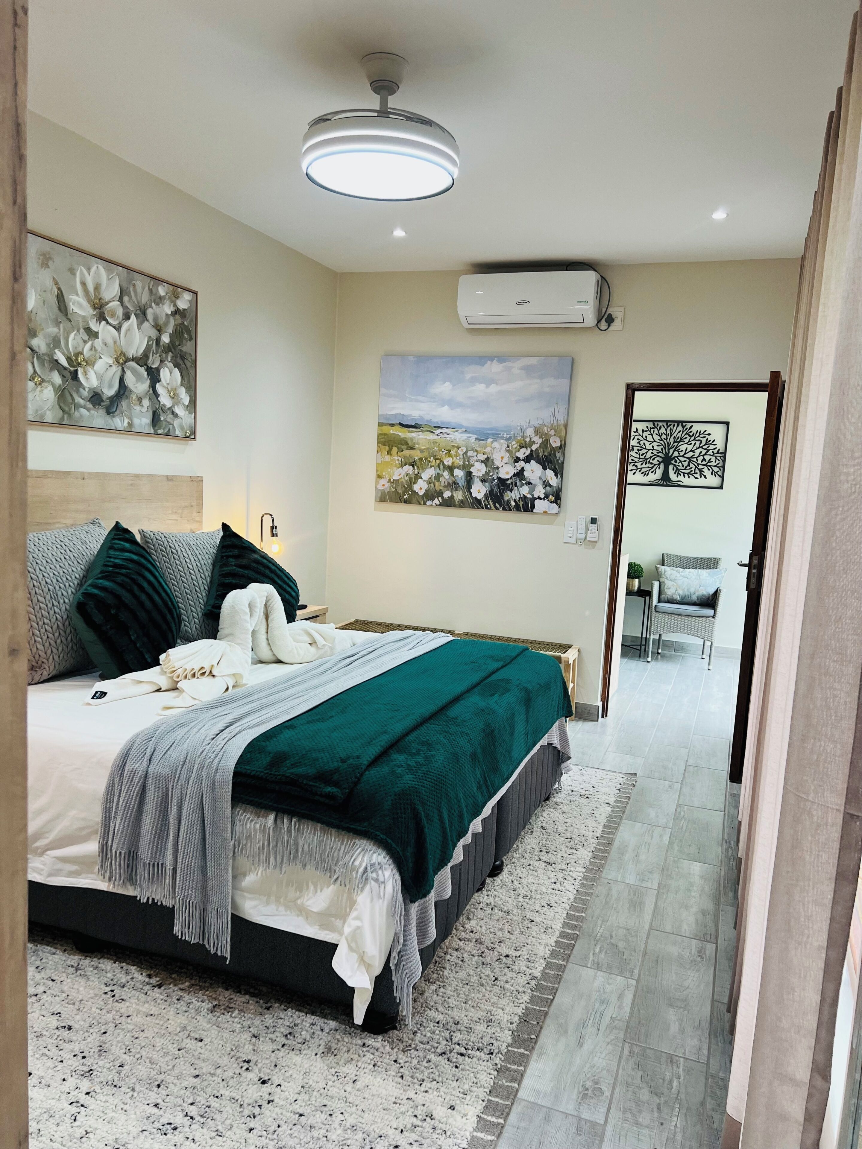 A bedroom with a bed, a painting, an air conditioning unit, and a view to another room.