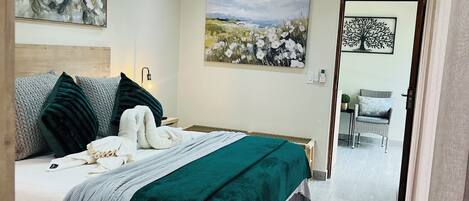 A bedroom with a bed, a painting, an air conditioning unit, and a view to another room.
