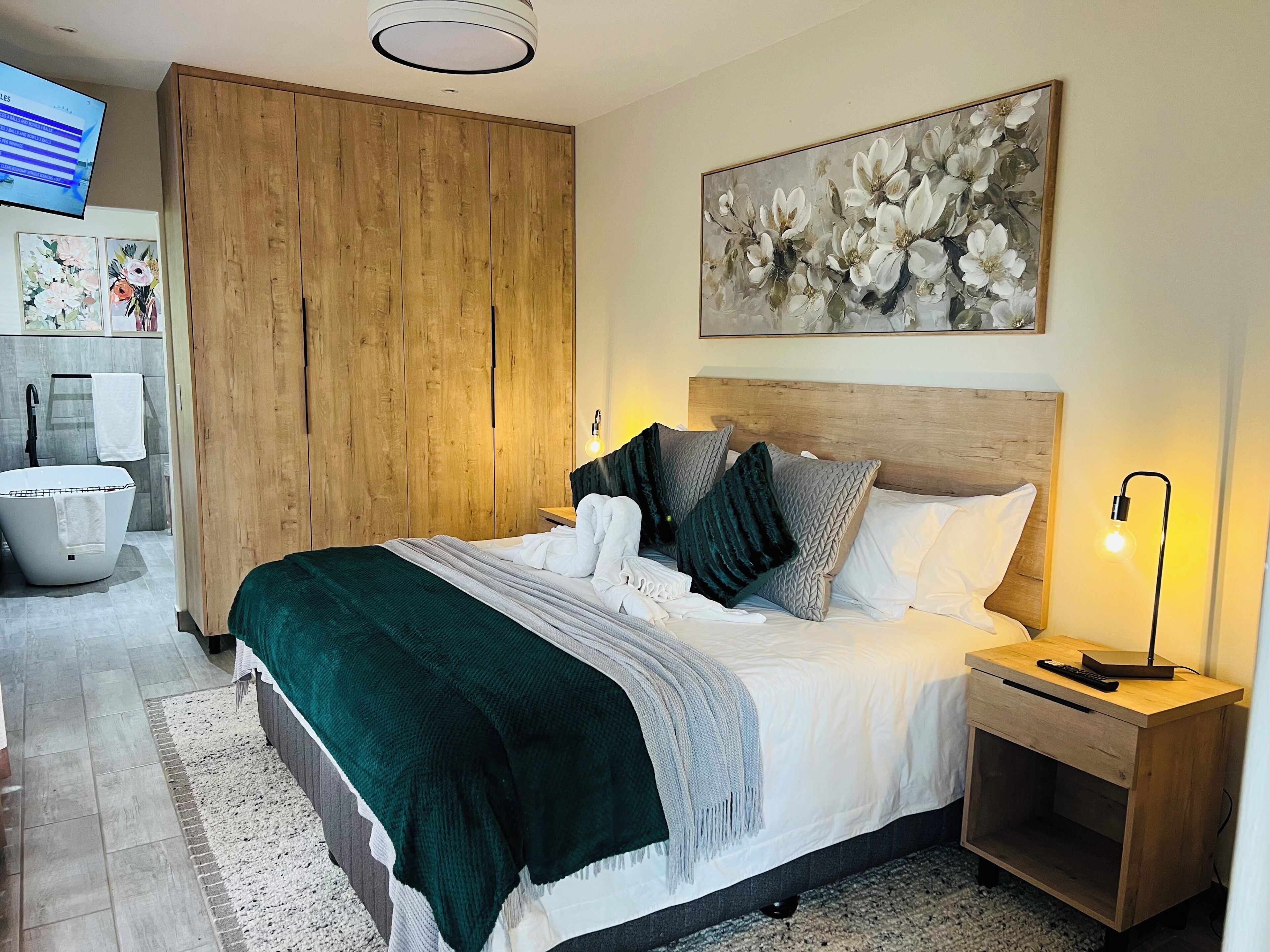 A modern bedroom with a bed, a nightstand, a wooden wardrobe, a painting, and a television.
