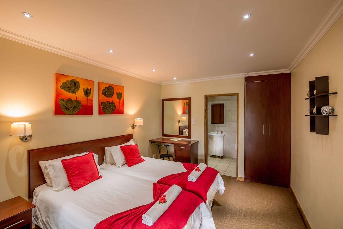 A hotel room with two beds, a desk, a mirror, and a wardrobe.