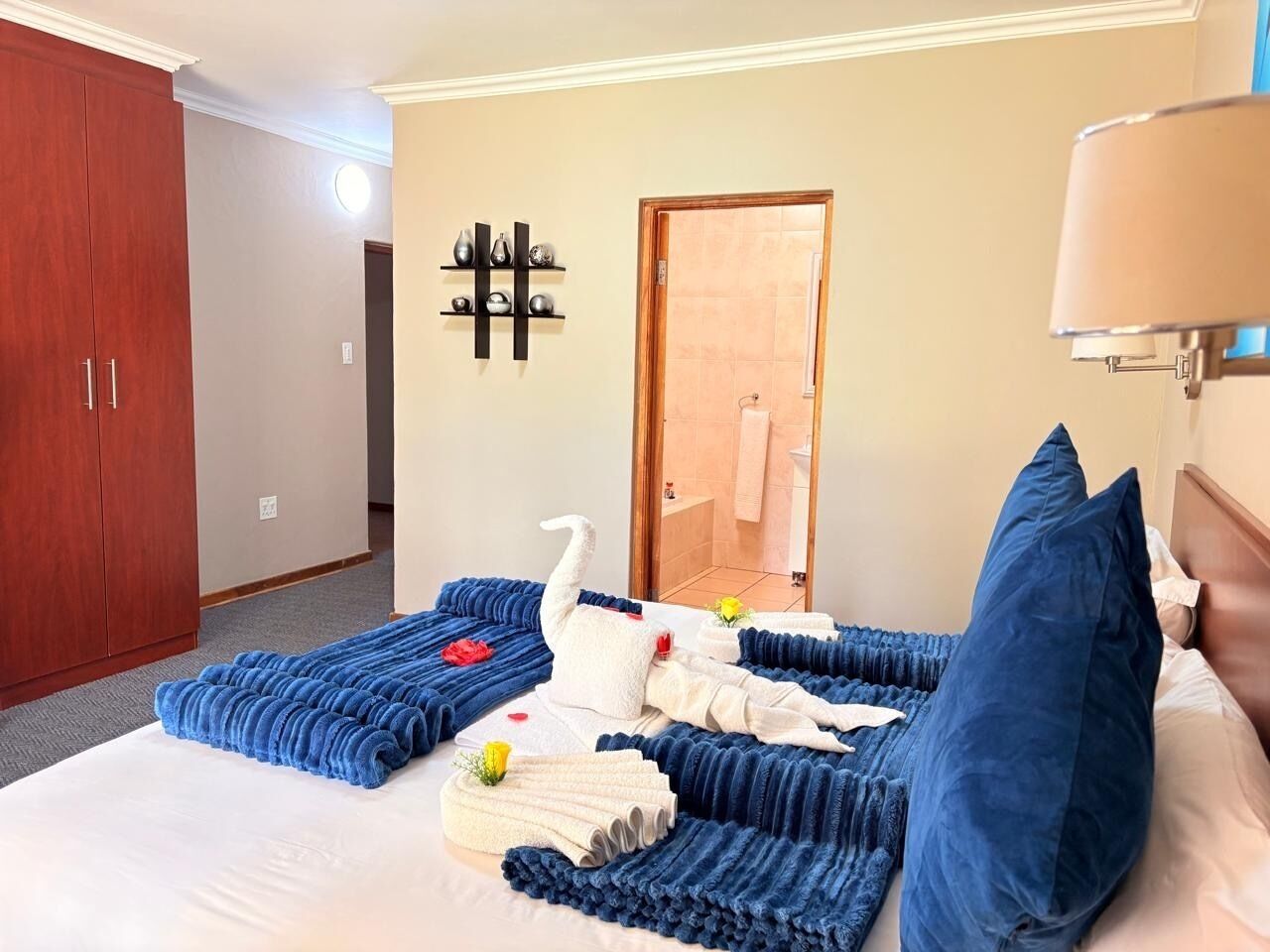 Een hotelkamer met een groot bed, een houten kledingkast, een wandplank met decoratieve objecten en een deur naar een badkamer.