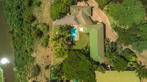 An aerial view of a property with a swimming pool, green-roofed buildings, and surrounding greenery.