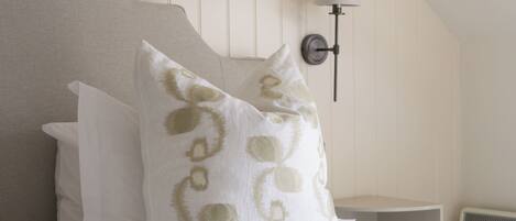 A bedroom with a bed, pillows, a wall-mounted lamp, and a sloped ceiling.