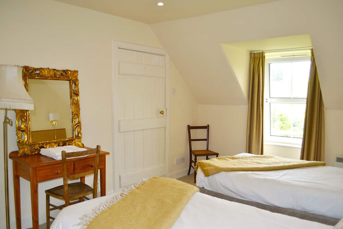 A bedroom with two beds, a wooden dresser, a mirror, a chair, and a window with curtains.
