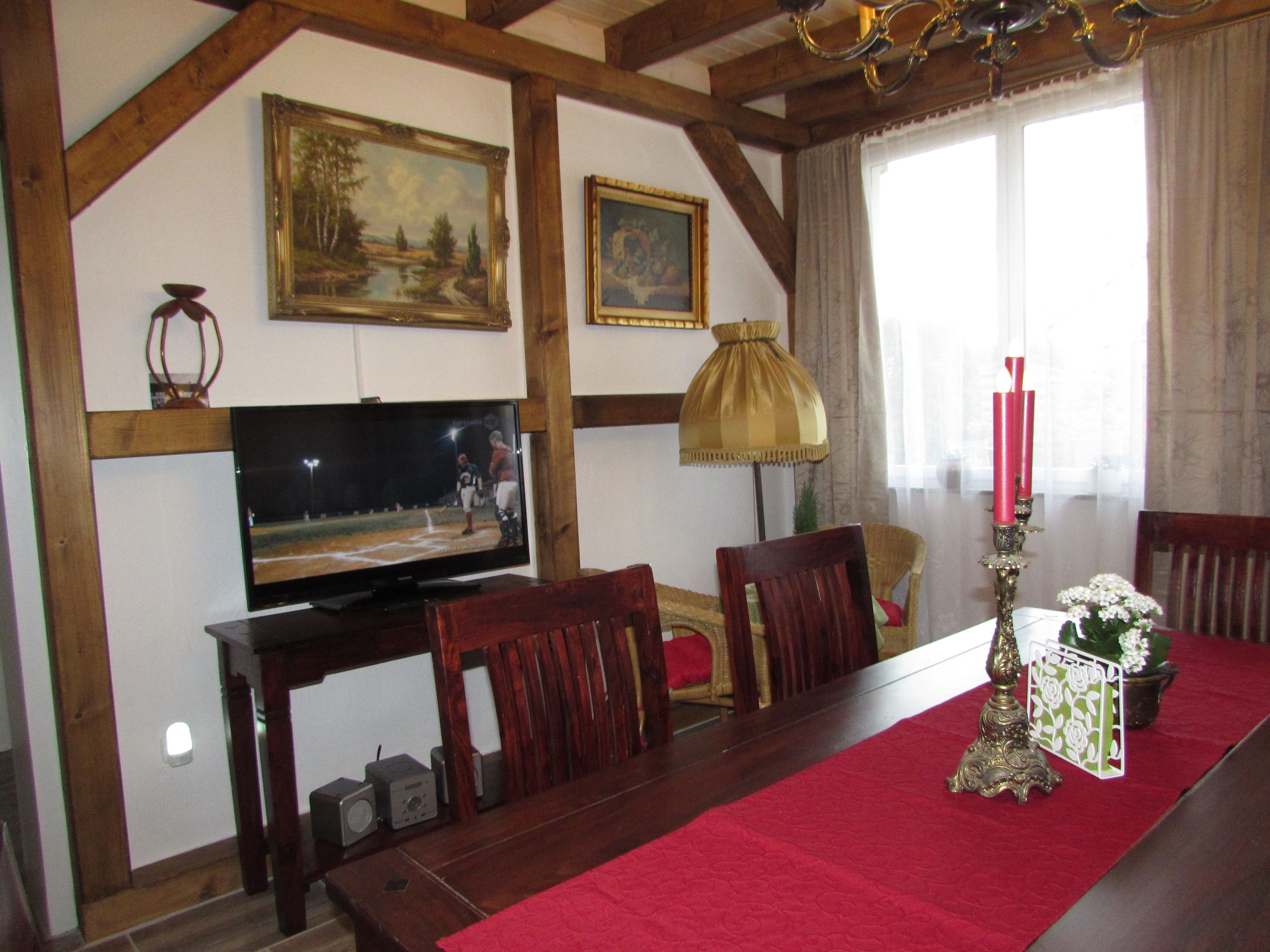 A dining area with a wooden table, chairs, a television, and framed artwork on the wall.