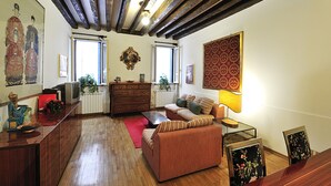 A living room with wooden flooring, a sofa, a coffee table, a TV, and a red rug. - Ca Maurice (Venice)