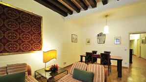 A living room with striped sofas, a glass coffee table, a dining table with chairs, and a large patterned rug. - Ca Maurice (Venice)