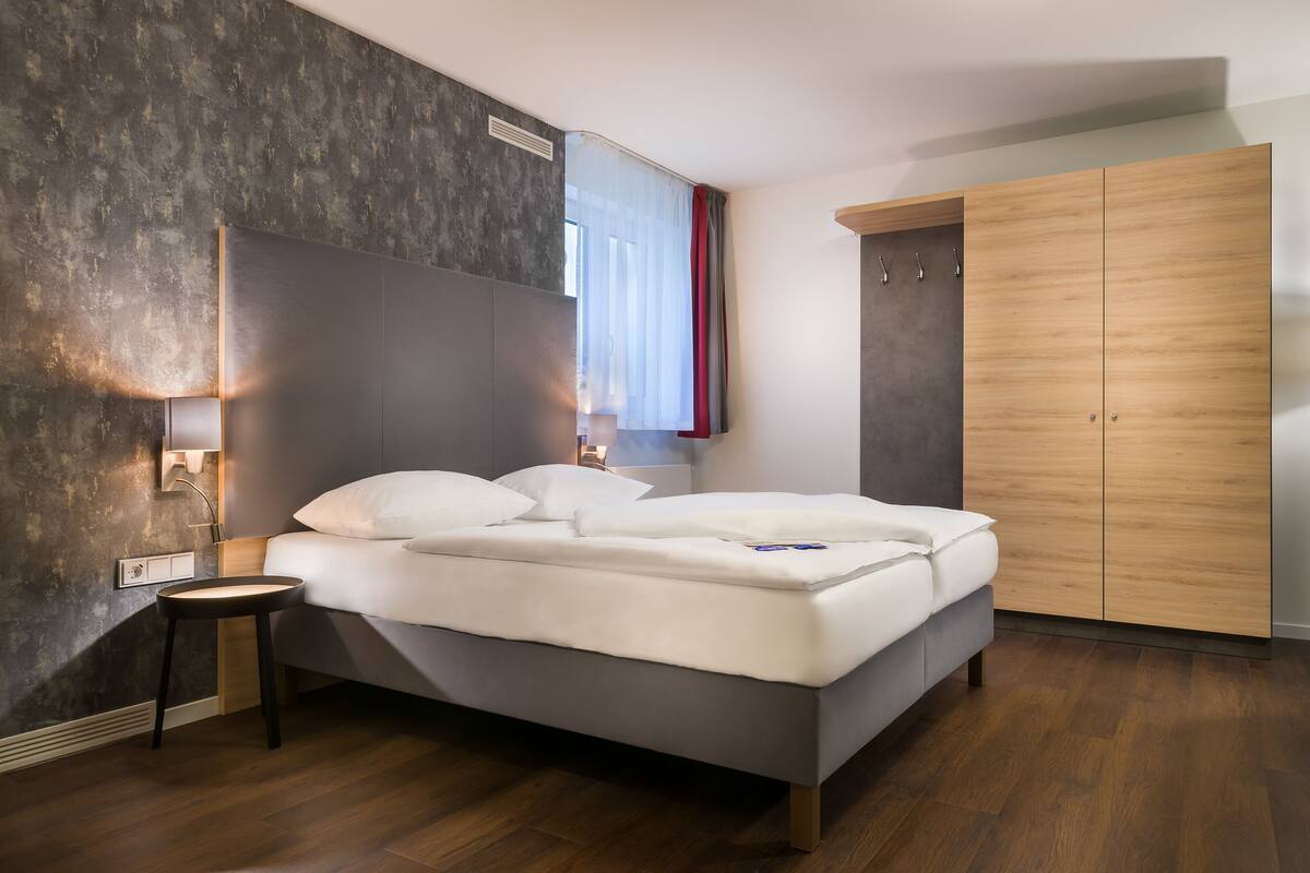 Een moderne slaapkamer met een bed, nachtkastje, wandlamp en een houten garderobe.