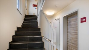 Een moderne trap met zwarte treden en witte leuningen, leidend naar een kamer met een houten deur en een bordje met het nummer 306.