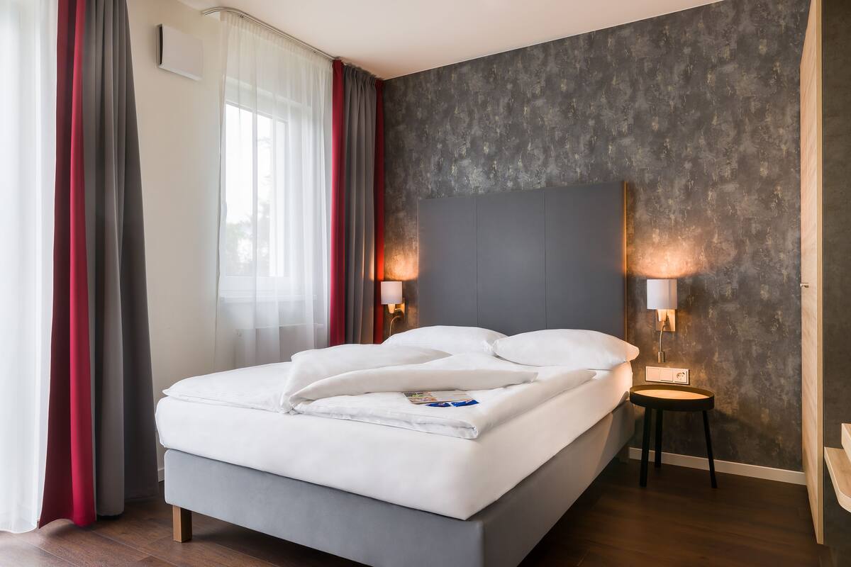 Een moderne hotelkamer met een groot bed, twee bedlampen, een donkere, structuurrijke wand en een houten vloer.