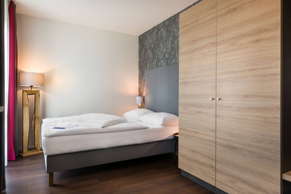 Een moderne slaapkamer met een bed, nachtkastje, lamp en kledingkast.