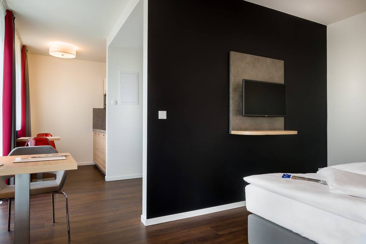 Een moderne hotelkamer met een zwarte accentmuur, een flatscreen televisie bevestigd aan de muur, een houten bureau met een stoel, en een bed met witte beddengoed.