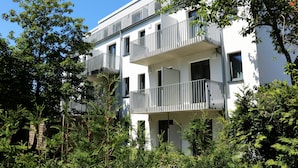 Een modern meerlaags gebouw met balkons, omringd door weelderige begroeiing.