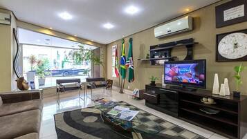 A modern hotel lobby with a glass coffee table, seating area, and a television displaying a sports event.