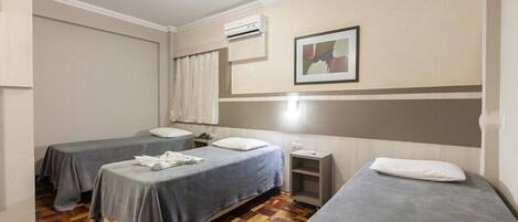 Habitación de hotel con dos camas, una mesita de noche, una pequeña mesa, aire acondicionado instalado en la pared y un cuadro enmarcado.