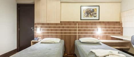 Habitación de hotel con dos camas, cabecera de madera, un cuadro, una mesita de noche y un escritorio pequeño.
