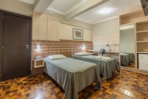 Habitación de hotel con dos camas, piso de madera, mesita de noche, escritorio con lámpara, espejo y armario.