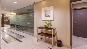 Un vestíbulo de hotel con mostrador de recepción, mampara de vidrio, una obra de arte enmarcada y una puerta.