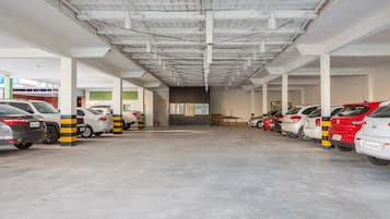 Un estacionamiento con varias filas de coches aparcados, pilares blancos con franjas amarillas y suelo de hormigón.