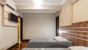 Habitación de hotel con dos camas, un televisor de pantalla plana montado en la pared y un equipo de aire acondicionado.