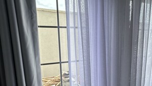 A window with sheer white curtains, a view of a building outside, and a concrete wall. - Bozcaada Arcadia (Bozcaada)