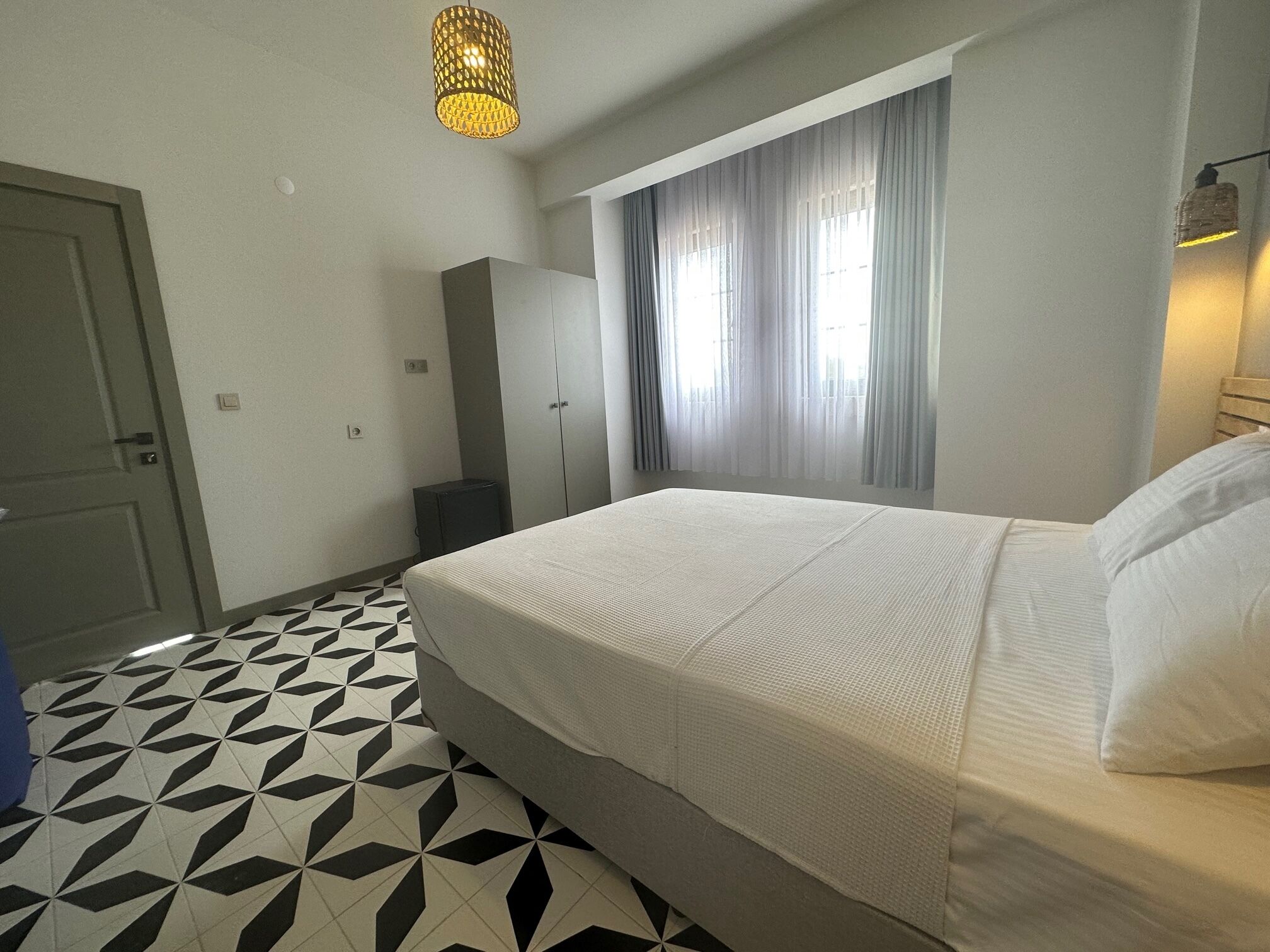 A hotel room with a bed, a wardrobe, a small table, and a window with curtains.