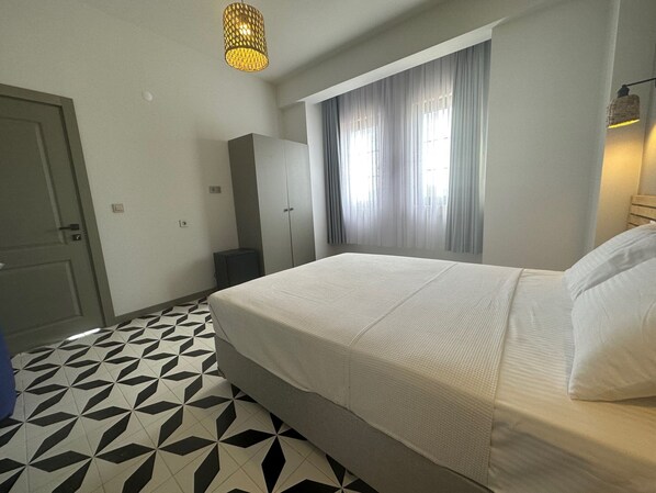 A hotel room with a bed, a wardrobe, a small table, and a window with curtains.