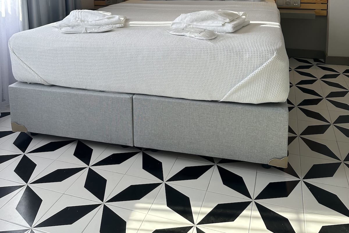 Un dormitorio moderno con una cama grande, cortinas grises y un suelo con estampado geométrico.