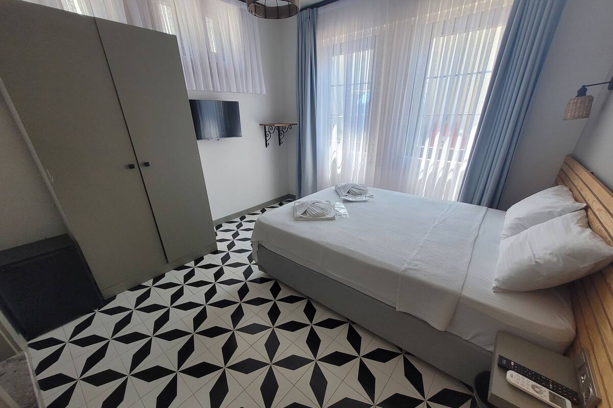 Habitación de hotel con cama, armario, televisor y suelo con estampado geométrico.