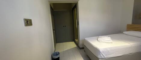 A hotel room with a bed, a trash bin, an air conditioning unit, and a door leading to another room.