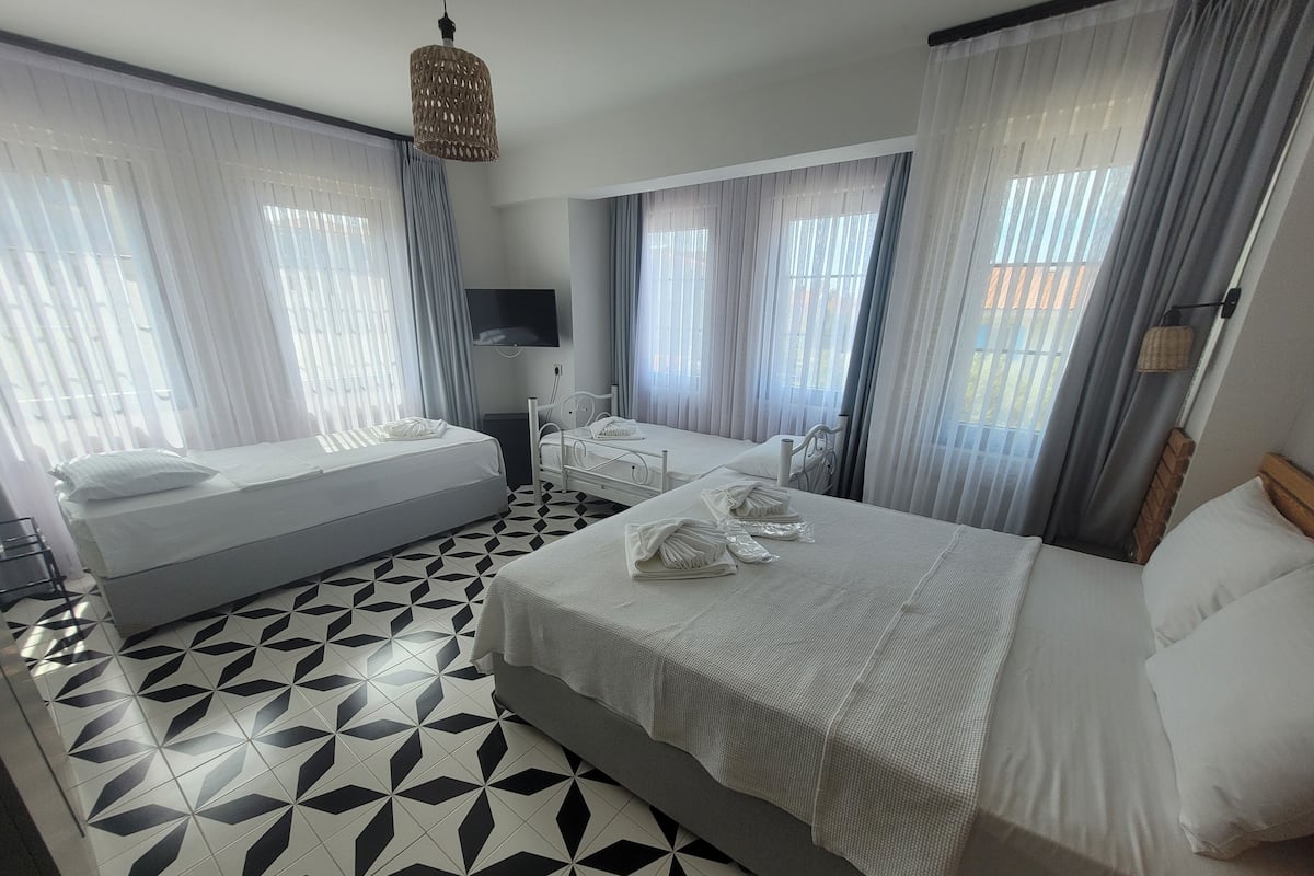 Una habitación de hotel con una cama grande, dos camas más pequeñas, un televisor y un suelo con diseño geométrico.