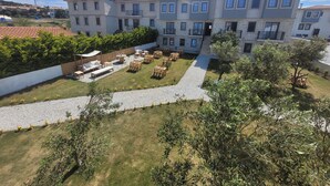 A multi-story building with a courtyard featuring outdoor seating and a gravel path. - Bozcaada Arcadia (Bozcaada)