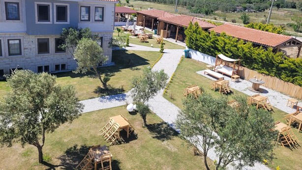A two-story building with a tiled roof, a paved courtyard, outdoor seating, and a view of rolling hills in the background. - Bozcaada Arcadia (Bozcaada)