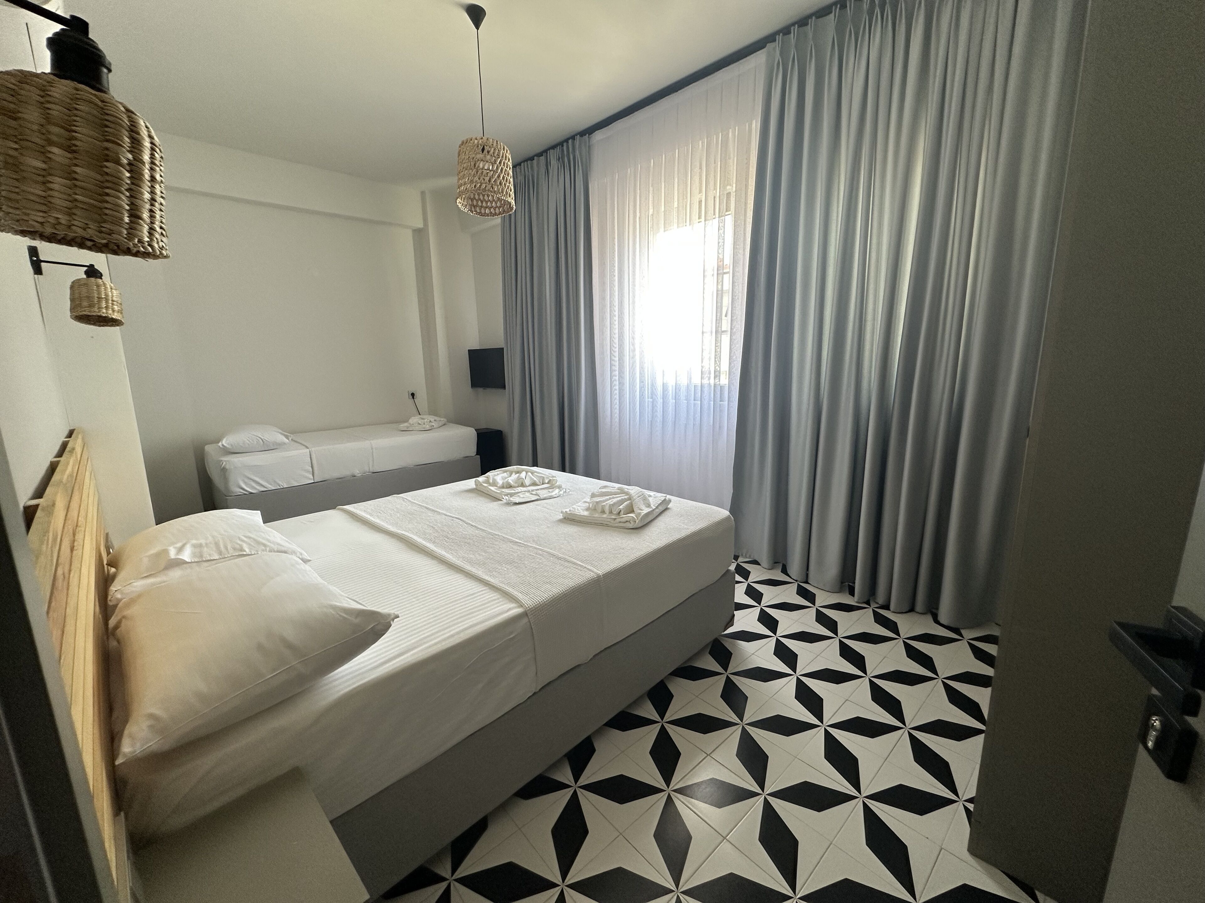A hotel room with a bed, a bedside table, a TV, and a window with curtains.