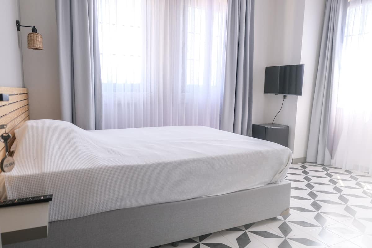 Una habitación de hotel moderna con una cama grande, un televisor de pantalla plana montado en la pared y un piso con estampado geométrico.