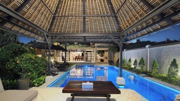 Uma área de piscina com pérgola, mobiliário de exterior e vista para uma casa ao fundo.