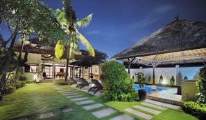 A resort with a pool, outdoor seating, and a thatched-roof structure.
