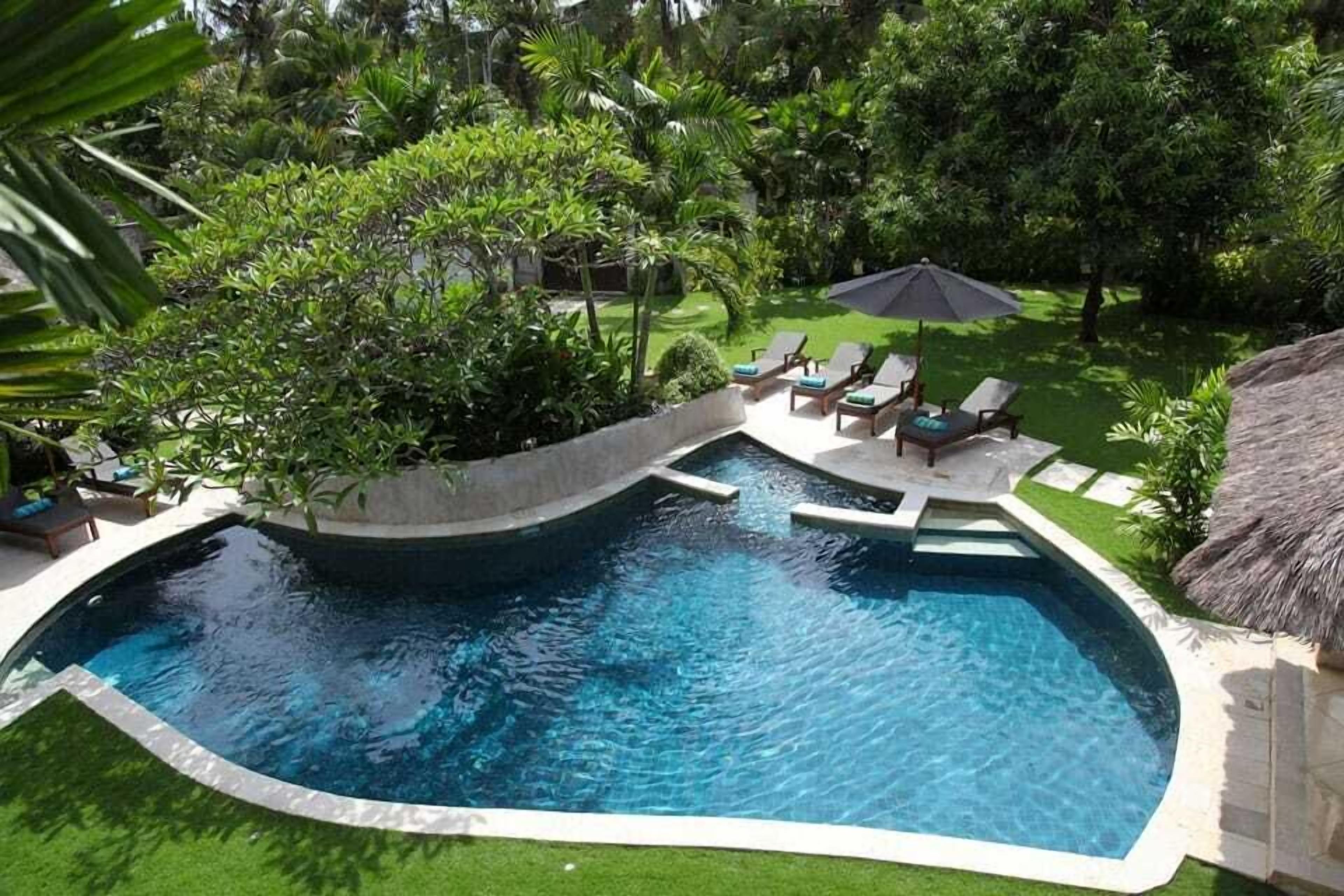 Ein Pool mit geschwungener Kante, umgeben von einem gepflegten Rasen und verschiedenen tropischen Pflanzen.
