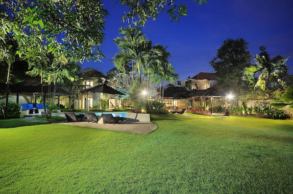 A well-lit outdoor area with a swimming pool, lounge chairs, and a grassy lawn.