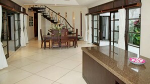 Uma sala de estar ampla com uma mesa de jantar, cadeiras, uma escada e janelas grandes.