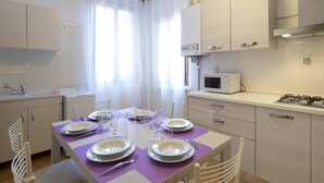 A modern kitchen with white cabinets, a dining table set for four, a microwave, and a gas stove. - Coco (Venice)