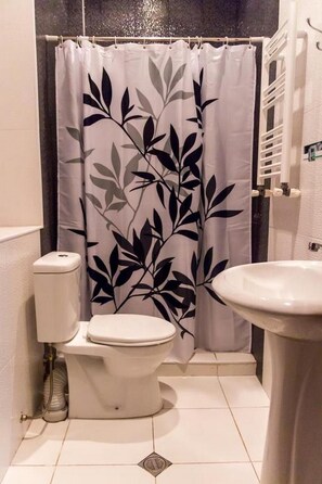 Un baño con inodoro, lavabo y cortina de ducha estampada con hojas.