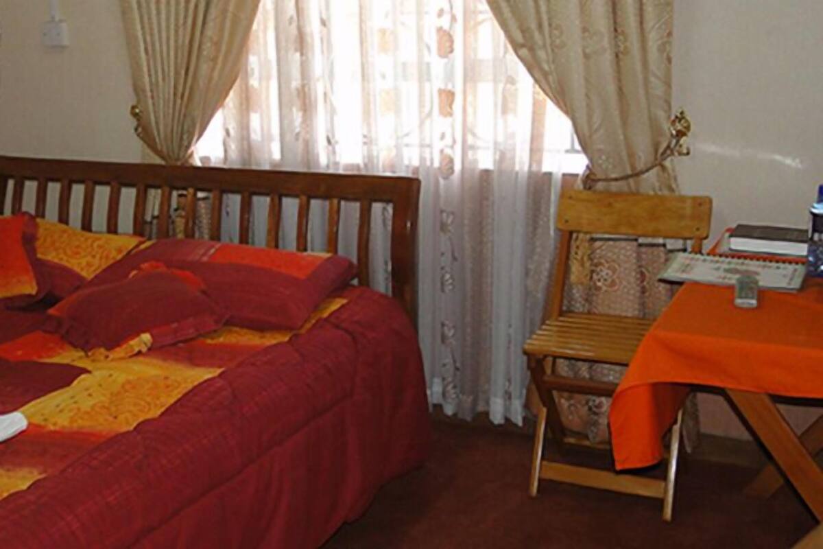 A bedroom with a bed, a chair, and a table with a book and a bottle.