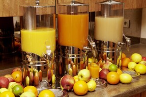 Un plan de travail de cuisine sur lequel reposent trois extracteurs de jus, chacun rempli d’un type de jus différent, entourés de divers fruits et d’un verre de jus.
