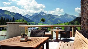 Une terrasse avec des meubles en bois, une vue sur les montagnes et un espace de stationnement avec des voitures.