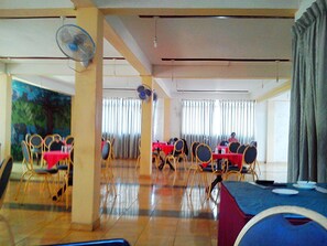 A dining area with tables and chairs, a fan, and a painting on the wall. - Hotel Elephant Lobby (Rambukkana)