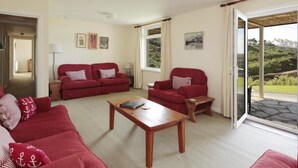 A living room with red sofas, a wooden coffee table, and a view through a glass door. - Green Door - Lower Tregudda (Port Isaac)