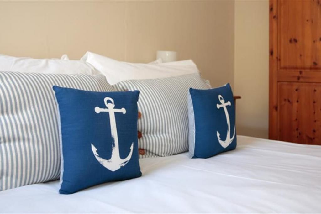 A bed with striped bedding and two pillows with anchor designs.